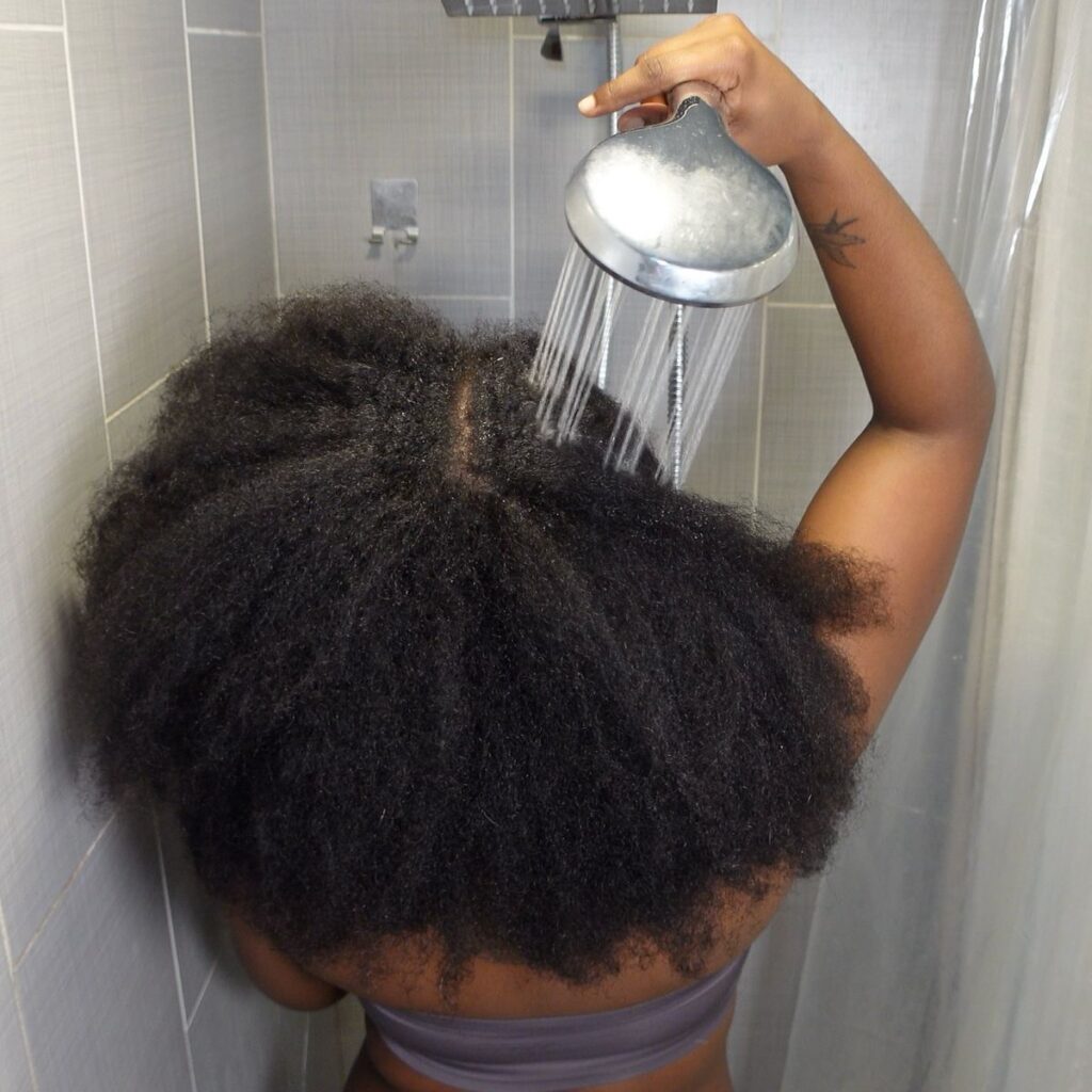a lady with a full Afro Hair pouring water on her hair in a bathroom