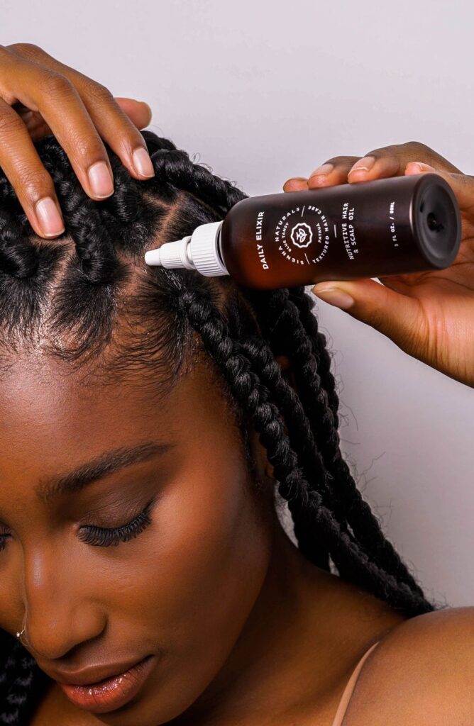 someone applying hair growth oil to her protective style