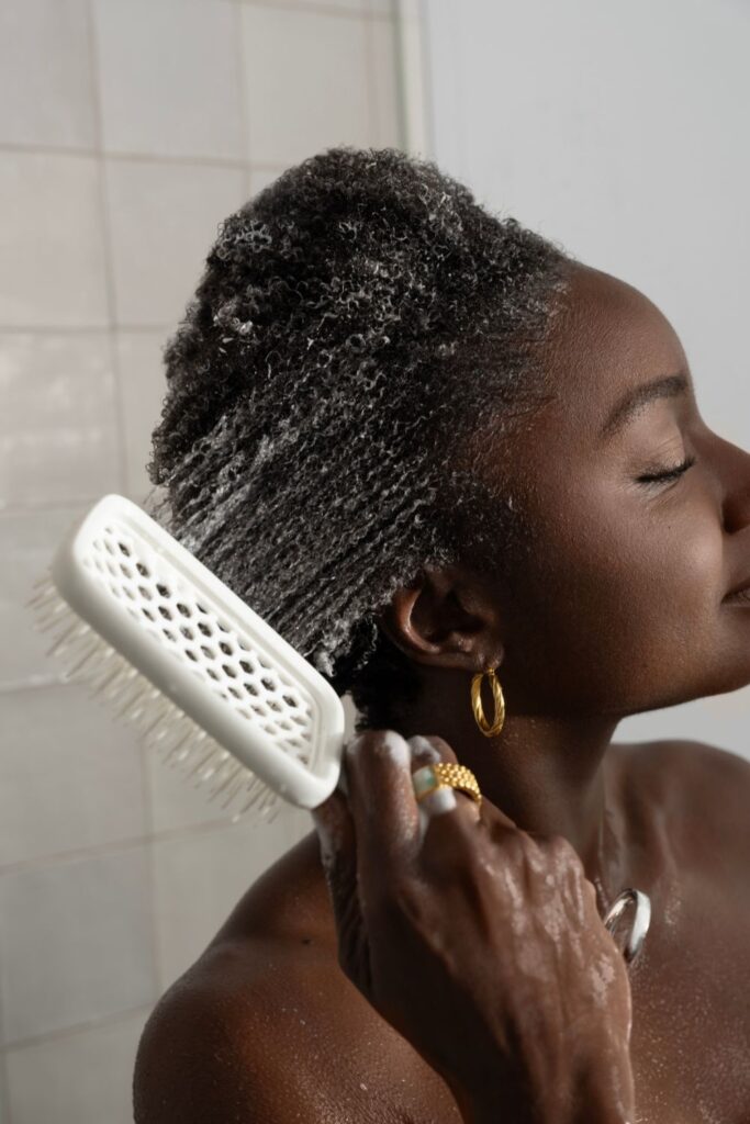a dark skinned lady combing her hair with a paddle brush while washing it