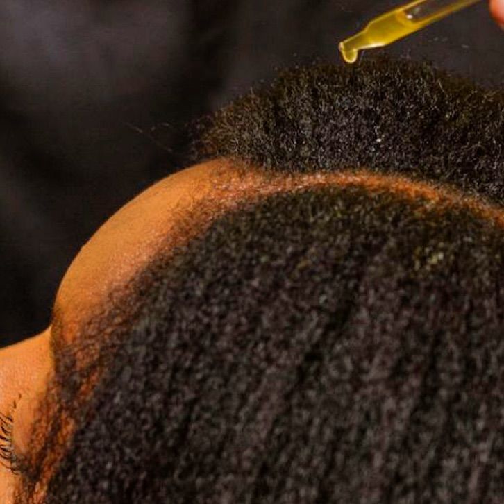 someone applying oil to her scalp as part of the ways to build healthy afro hair