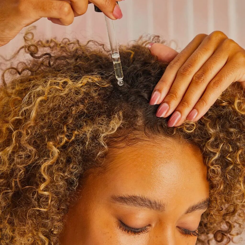 someone applying hair growth oil to her curly hair