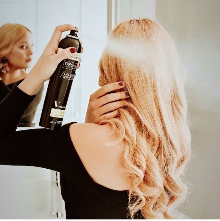 someone spraying hair product on her afro hair under wig