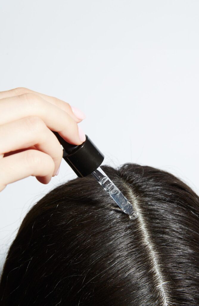 someone applying oil to her afro hair under wig