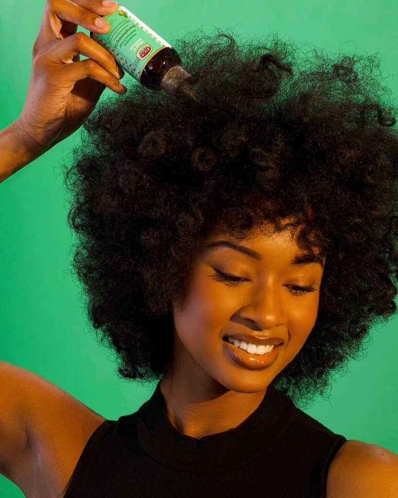 someone applying hair product to her hair as summer hair care routine for afro hair