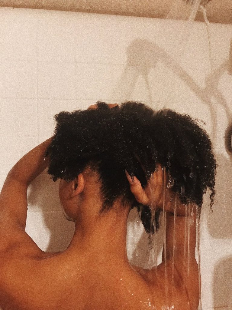 someone rinsing her hair with cold water as a way to protect afro hair from humidity